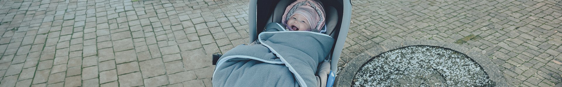 Kind lacht in Kinderwagen mit grauer Decke